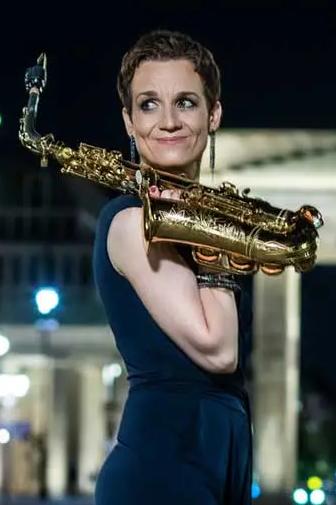 Katja Lau holding a saxophone in front of Brandenburg Gate at night.