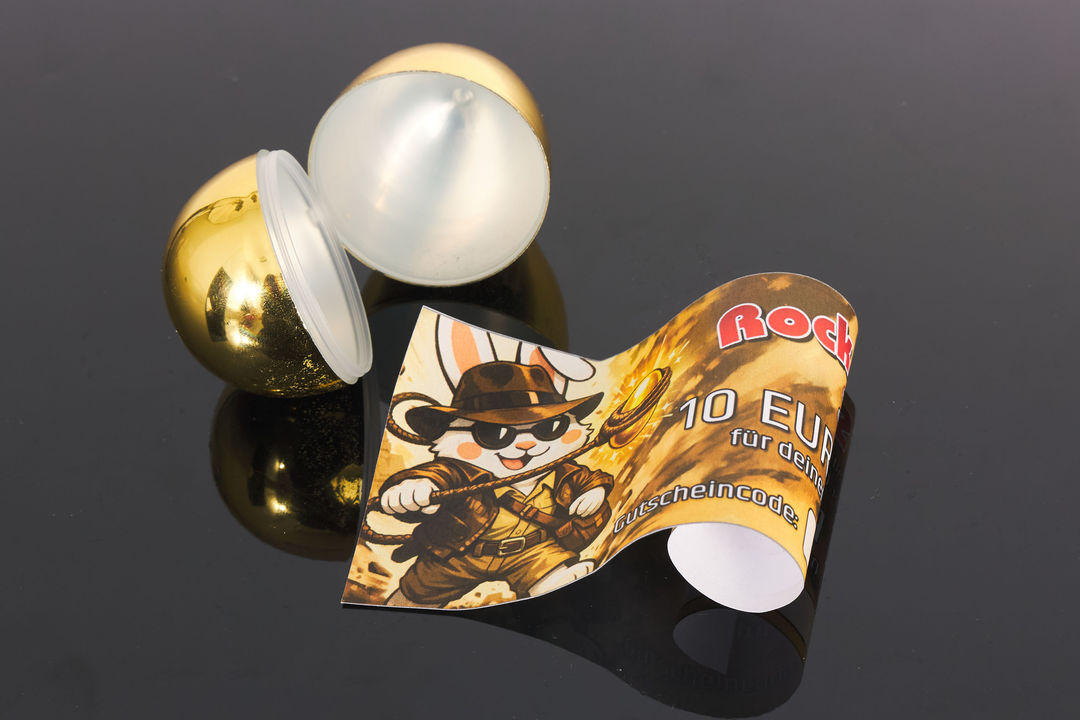 Zusammengerollter 10 Euro Einkaufsgutschein vor geöffnetem goldenem Ei