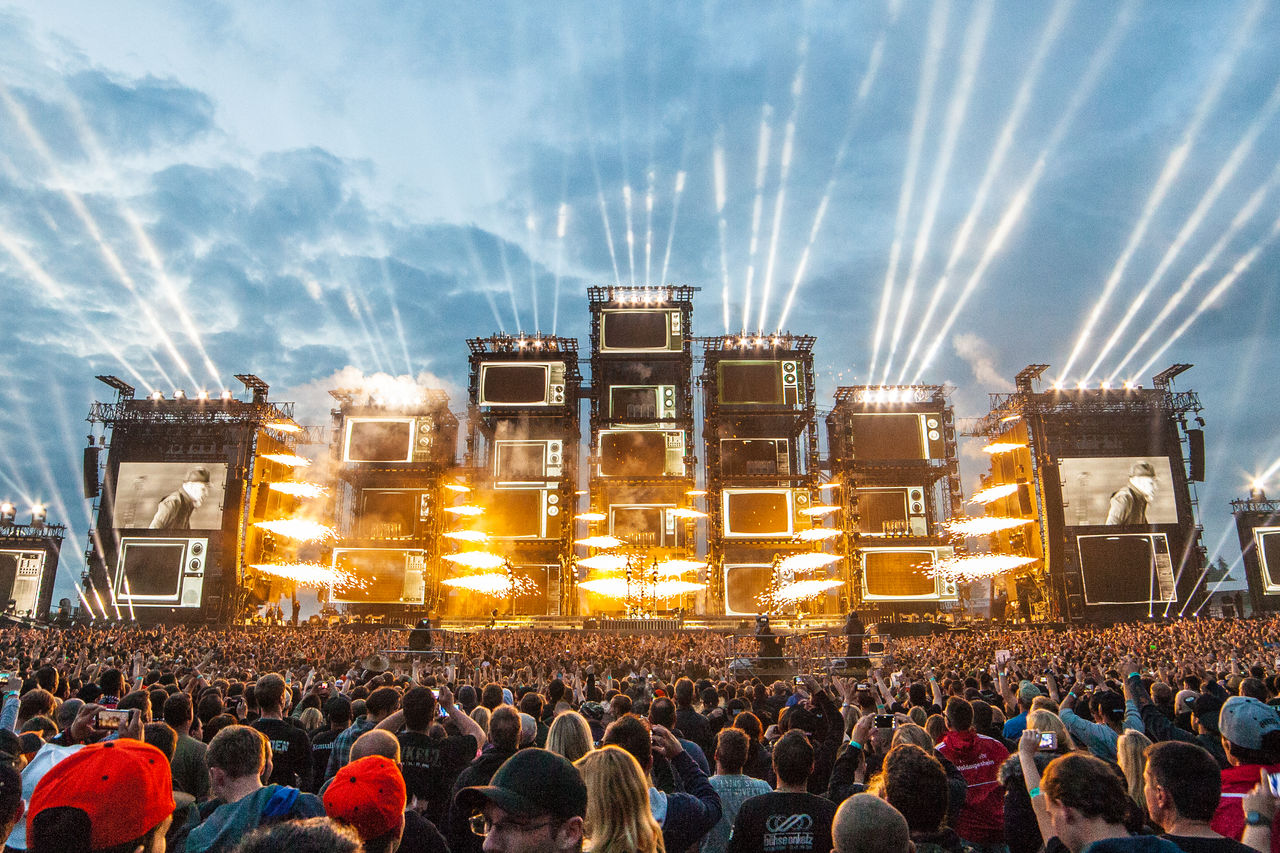 Festival stage at night with pyrotechnics, video walls, and light show in front of a large audience